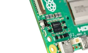 Zbliżenie na zieloną płytkę drukowaną Raspberry Pi 6 z widocznym przyciskiem, złączami i logo.