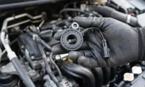 Ręka w czarnej rękawiczce trzyma nowy knock sensor, gotowy do montażu w silniku samochodu.