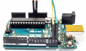 Płytka Arduino z podłączonymi przewodami. Programista tworzy pętlę `while` do sterowania urządzeniami.