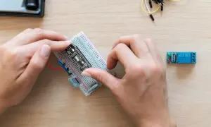 Ręce montują płytkę z czujnikiem zbliżeniowym Arduino na płytce stykowej. Obok leży moduł przekaźnika.