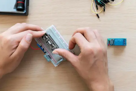 Ręce montują płytkę z czujnikiem zbliżeniowym Arduino na płytce stykowej. Obok leży moduł przekaźnika.