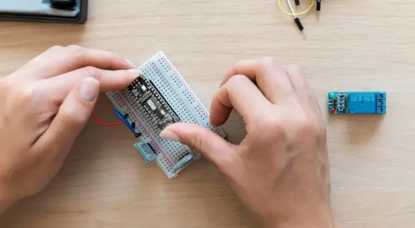 Ręce montują płytkę z czujnikiem zbliżeniowym Arduino na płytce stykowej. Obok leży moduł przekaźnika.