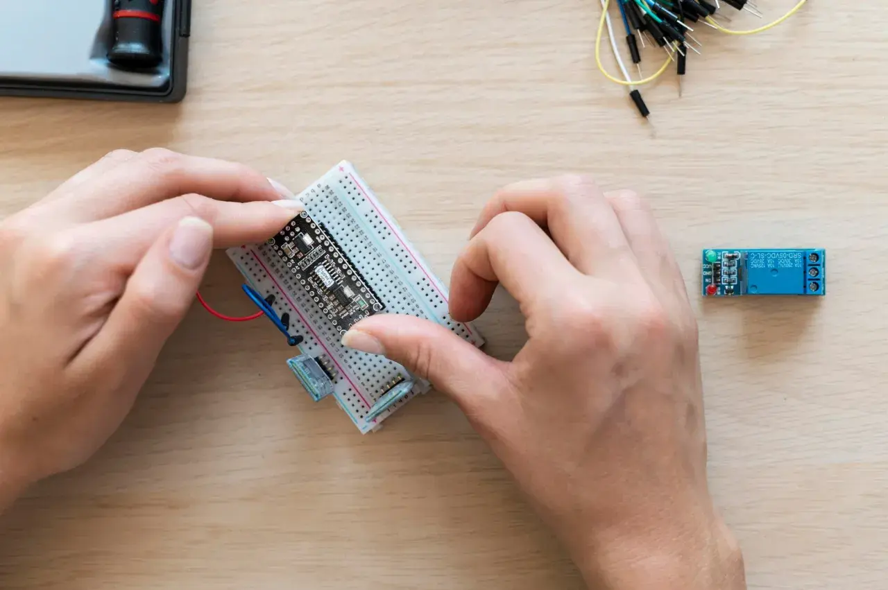 Ręce montują płytkę z czujnikiem zbliżeniowym Arduino na płytce stykowej. Obok leży moduł przekaźnika.