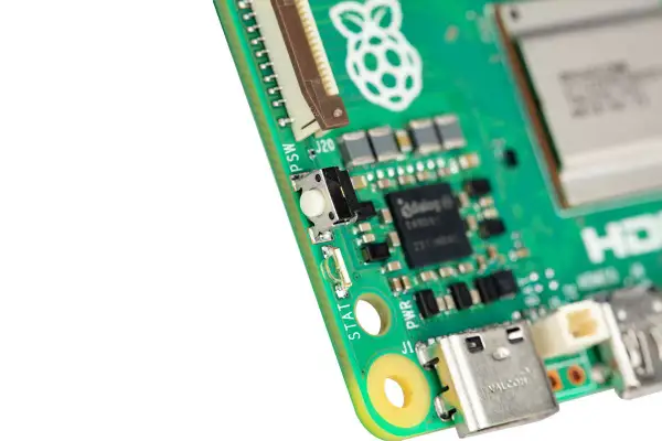 Zbliżenie na zieloną płytkę drukowaną Raspberry Pi 6 z widocznym przyciskiem, złączami i logo.