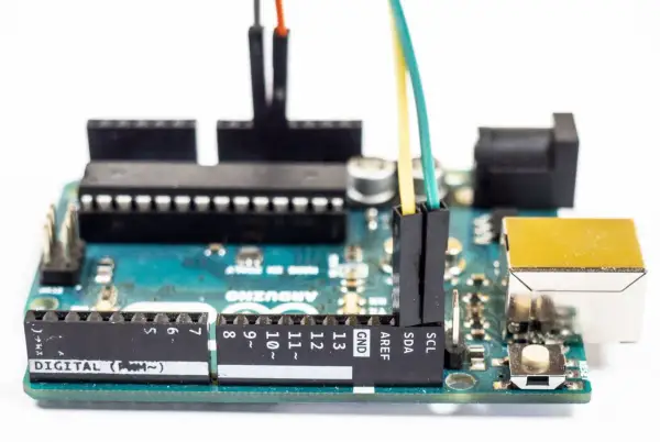 Płytka Arduino z podłączonymi przewodami. Programista tworzy pętlę `while` do sterowania urządzeniami.