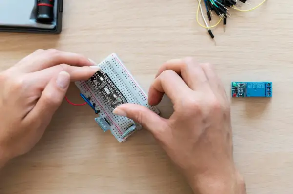 Ręce montują płytkę z czujnikiem zbliżeniowym Arduino na płytce stykowej. Obok leży moduł przekaźnika.